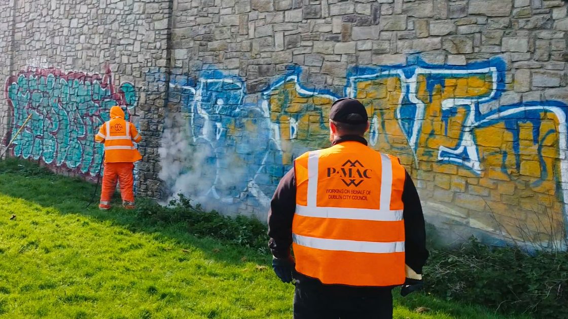 PMAC operatives removing large graffiti from stone wall